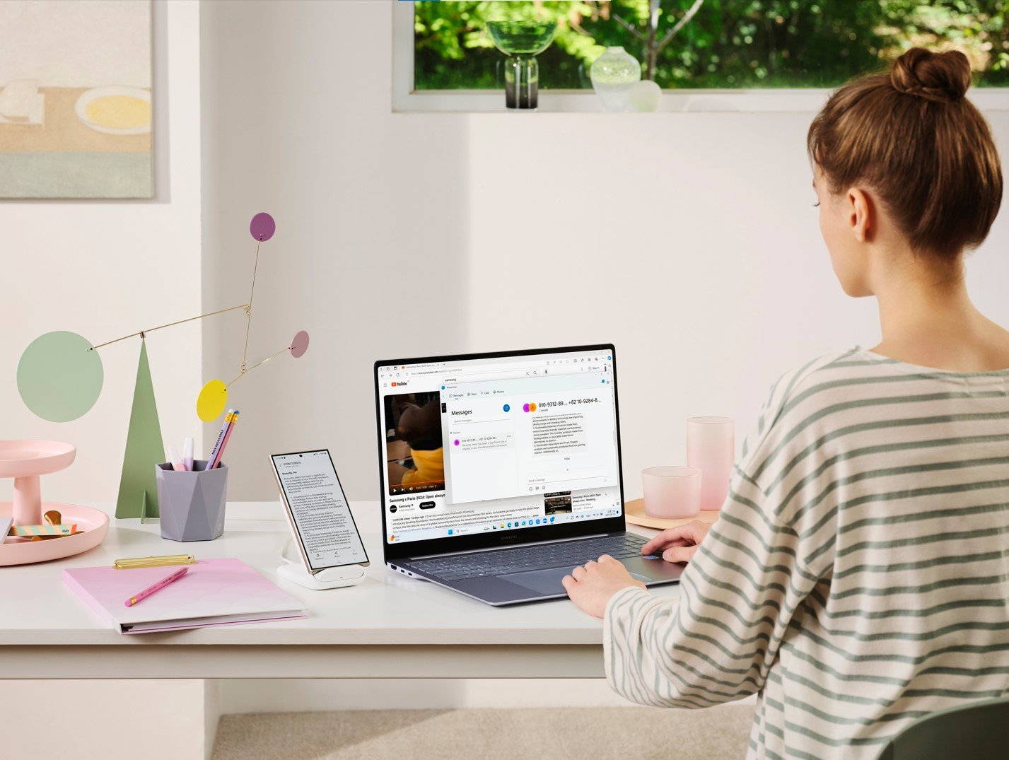 Woman working on the Galaxy Book4 Edge laptop at a modern home office setup A person using the Galaxy Book4 Edge laptop at a modern, stylish desk setup with a tablet and stationery, showcasing the laptop's sleek design and advanced features.